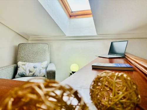 Luminoso espacio de trabajo en ático de Baiona con claraboya, escritorio con portátil, sillón e iluminación natural