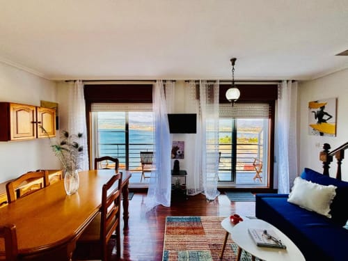 Apartamento luminoso en Baiona con vistas al mar, mesa de comedor de madera, sofá azul, TV y terraza con vistas a la costa