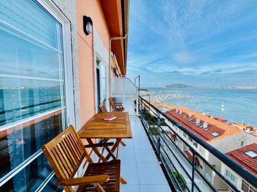 Terraza de apartamento junto al mar en Baiona con sillas de madera con vistas a la bahía y veleros