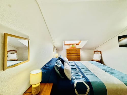 Acogedor dormitorio en buhardilla del apartamento de Baiona con tragaluz, cómoda de madera, ropa de cama azul y espejo