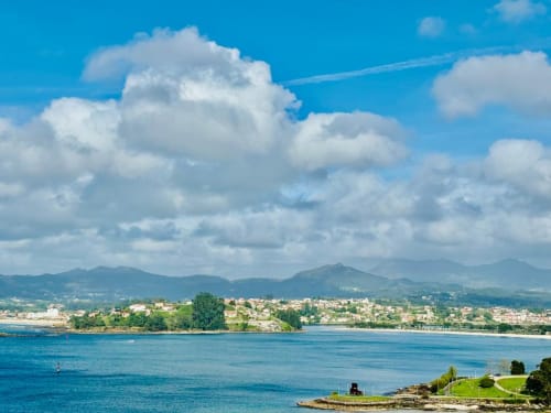 Vista desde la terraza de Holibai Miudiño: pueblo costero de Baiona, mar azul y montañas