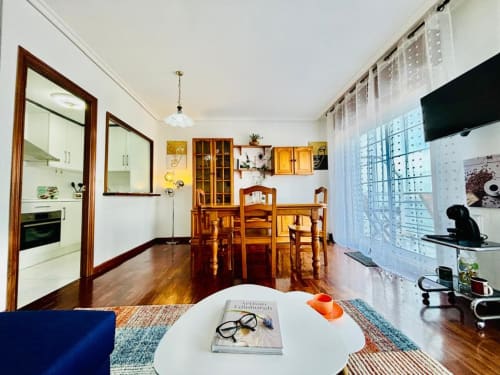 Sala de estar moderna en Baiona con mesa de comedor de madera, cocina, TV y acceso a balcón con vistas al mar