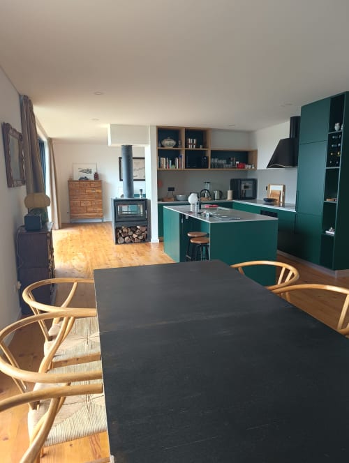 Cozinha moderna com armários verdes, mesa de jantar preta, cadeiras de madeira e lareira de pedra em casa de campo no Vale do Douro