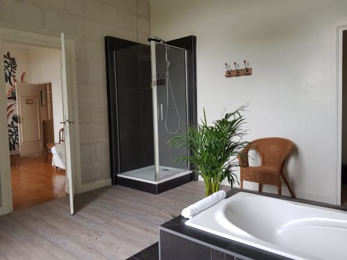 Spacious bathroom at Domaine de l'Oie Rouge with bathtub, rainfall shower, sink, and wicker chair in Gennes-Val-de-Loire