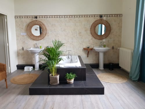 Spacious spa-style bathroom with dual sinks, black soaking tub, decorative mirrors, and potted plants at Domaine de l'Oie