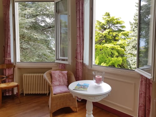Cozy sunlit bedroom corner with wicker chair, side table, and scenic garden views at Domaine de l'Oie Rouge,