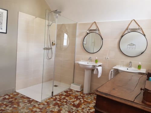 Modern en suite bathroom at Domaine de l'Oie Rouge with walk-in shower, dual pedestal sinks, and round mirrors