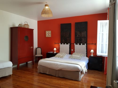 Bedroom with vibrant red walls, black headboards, white bedding, wooden floor, and traditional Asian-inspired decor at