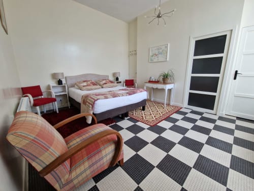 Spacious bedroom with red and cream decor, checkered floor, queen bed, armchair, and en-suite bathroom at Domaine de l'Oie