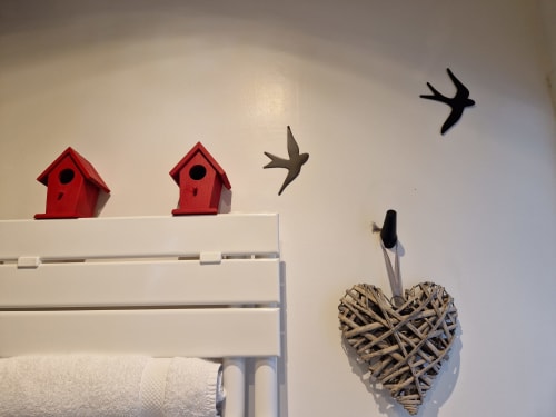 Bathroom decor in Coriandre room: red birdhouses, flying bird silhouettes, woven heart decoration with towel rack at Domaine