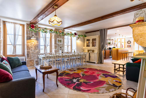 Spacieux séjour ouvert à La Maison George avec table de salle à manger, tapis coloré, murs en pierre et mobilier élégant