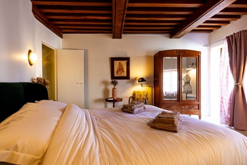 Elegant bedroom at La Maison George with exposed wooden beams, cream bedding, wooden wardrobe, and warm lighting
