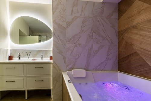 Luxury bathroom at La Maison George with illuminated oval mirror, marble walls, sage cabinetry, and purple-lit Jacuzzi tub in