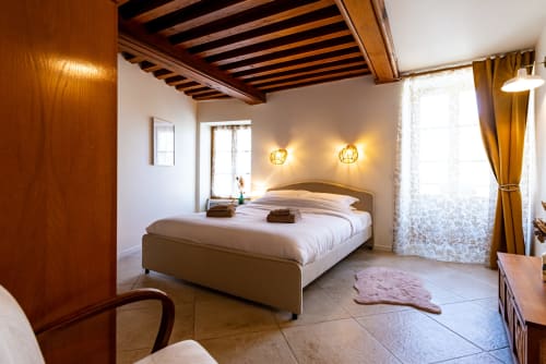 Bright bedroom at La Maison George with queen bed, wooden beams, warm lighting, and large windows overlooking Flavigny sur