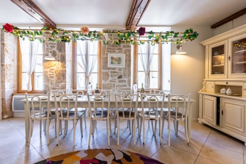 Elegant dining room at La Maison George with long table, white chairs, stone walls, and floral garland decoration
