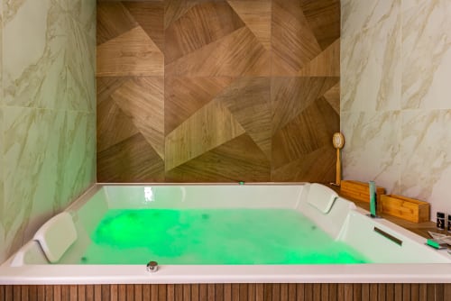 Luxurious green-lit Jacuzzi bathtub with herringbone wood wall backdrop at La Maison George apartment in Flavigny sur