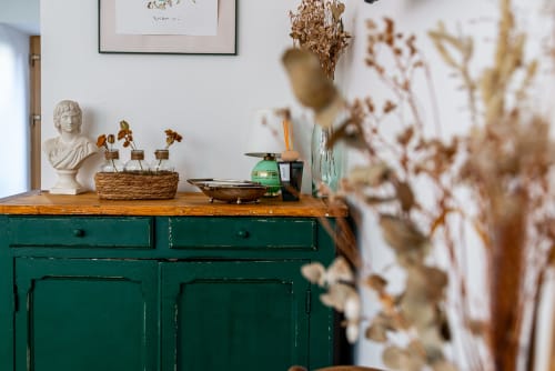 Stylish green dresser with wooden top displaying decorative bust, dried flowers, and home décor in Logis Camille apartment at