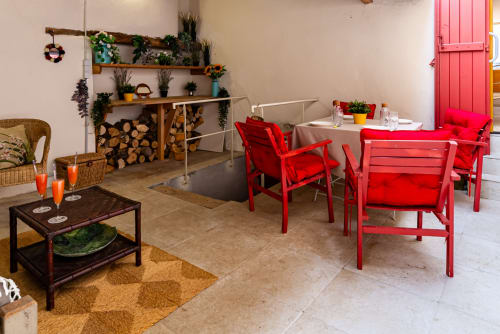 Bright living area with red chairs, wooden shelves, plants, and dining setup at La Maison George hotel apartment in Flavigny