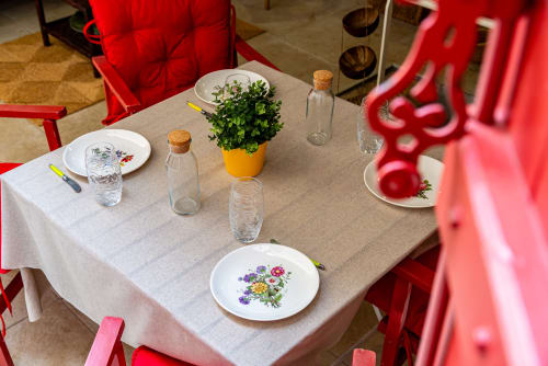 Elegant dining setup at La Maison George with beige tablecloth, floral plates, fresh green plant, and bright red chairs in