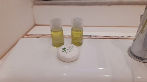Amenità bagno della Michelangelo Suite Roma: due bottiglie di cosmetici gialli e sapone sul bancone bianco del lavabo