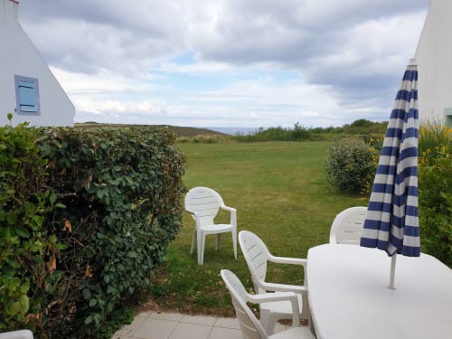 Coin détente en plein air aux Locations Loc'Maria sur Belle Île en Mer avec chaises blanches, parasol rayé et vues côtières pittoresques