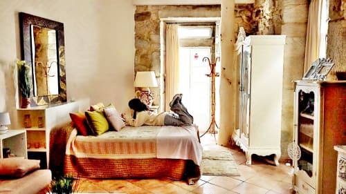 Dormitorio loft Peperete en Baiona con cama, espejo, cojines coloridos, armario y acceso a balcón con vistas a la ciudad