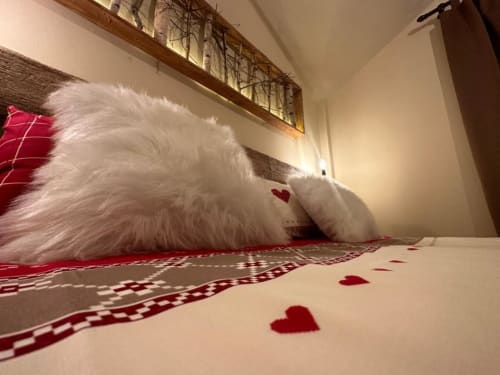 Fluffy white cat rests on red and white patterned bedding with heart decorations in Hotel Le Clou's Superior King Room