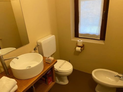 Bathroom at Hotel Le Clou in Arvier with round sink, toilet, bidet, wooden vanity, and window with city view