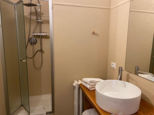 Modern bathroom in Hotel Le Clou with glass shower enclosure, white round sink, and folded towels on wooden shelf