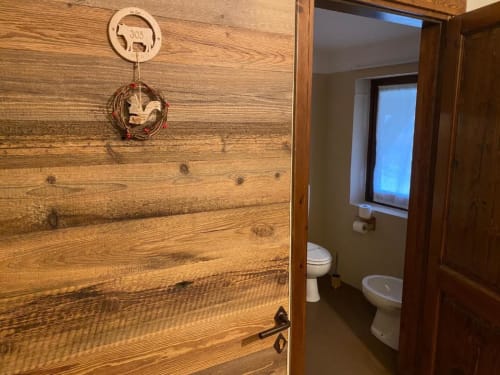 Wooden door to bathroom at Hotel Le Clou, showing toilet, bidet, and window in Arvier, Italy