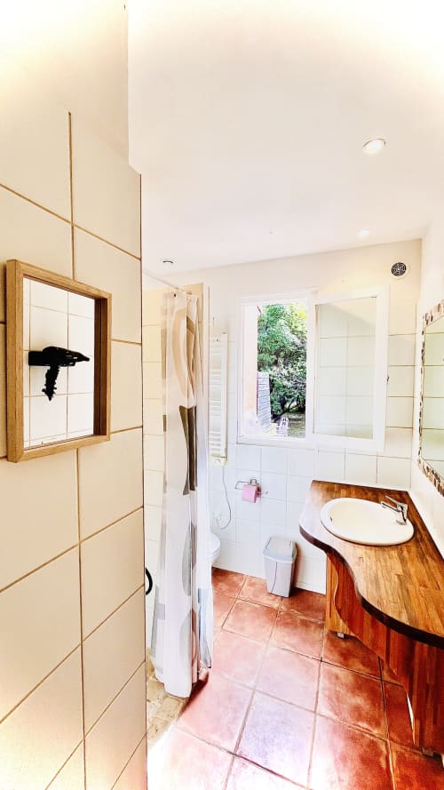 Salle de bains lumineuse de la villa Le Maquis Plage avec meuble vasque en bois, carrelage blanc et vue sur le jardin