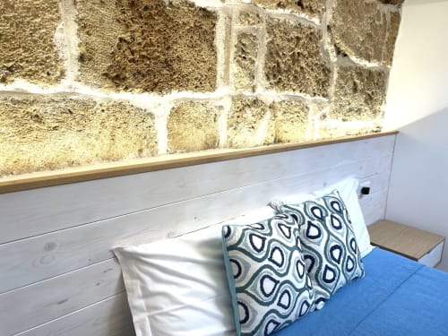 Cozy bedroom corner at Catalogna10 Rooms e Loft in Alghero with patterned pillow, blue bedding, white wooden headboard, and