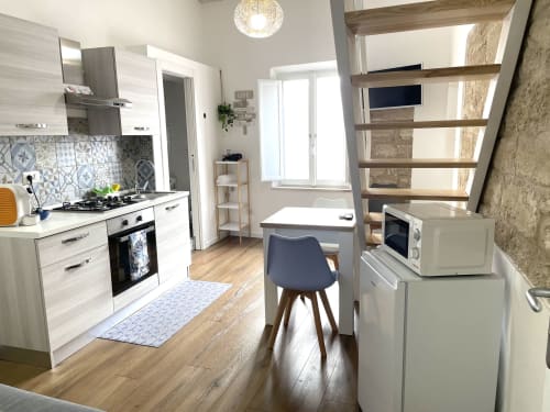 Modern kitchen-living space at Catalogna10 Rooms e Loft in Alghero with white cabinetry, gas stove, dining table, and wooden