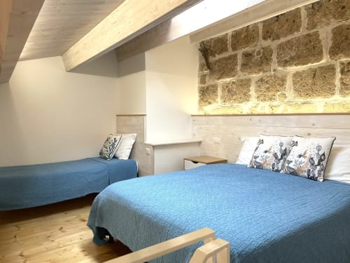 Modern loft bedroom at Catalogna10 in Alghero with blue beds, exposed stone, skylight, and wooden beams
