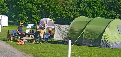 Family camping at Postwood Gardens Campsite in Kentisbeare with green tunnel tents, caravan, and outdoor seating area