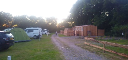 Postwood Gardens Campsite in Kentisbeare with tent, camper vans, wooden lodge and gravel path at dusk