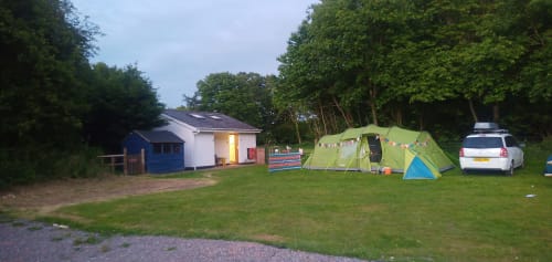 Postwood Gardens Campsite in Kentisbeare with green tent, static caravan, lodge buildings and parked car on grassy field