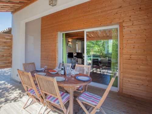 Terrasse couverte avec table et chaises en bois à la villa Le Maquis Plage en Corse, vue sur les jardins