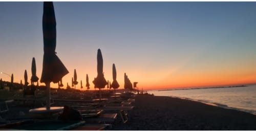 Tramonto sulla spiaggia di Le Vajane a Torino di Sangro con ombrelloni chiusi sagomati contro il cielo arancione