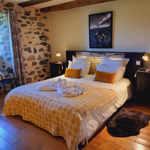 Chambre zen au Mas De Rigoulac avec lit king-size, accents orangés, mur en pierre et vue sur le jardin en Aubrac