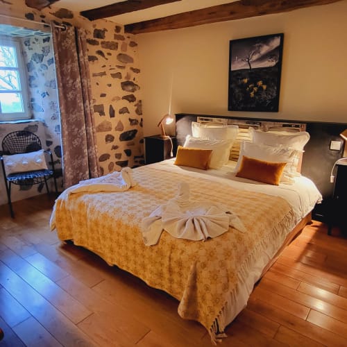 Chambre zen au Mas De Rigoulac avec literie dorée, murs en pierre, poutres en bois et vue sur le jardin