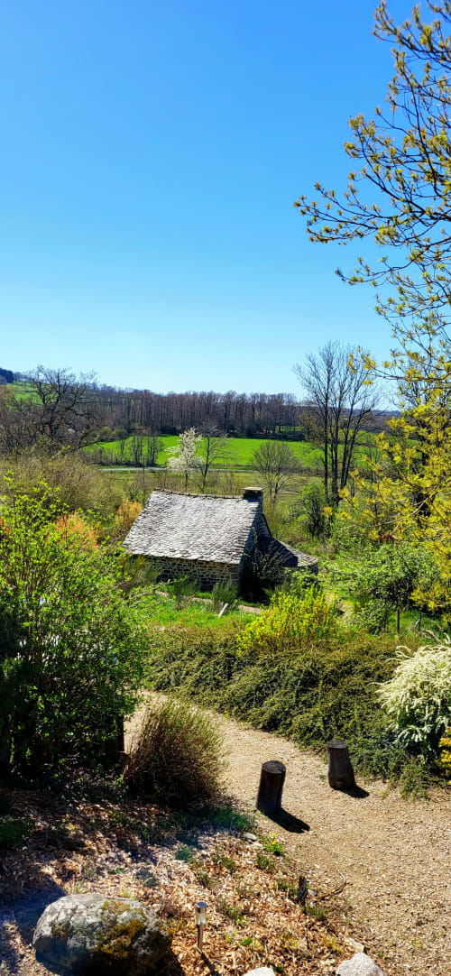 Chaumière en pierre avec vue sur le jardin du Mas De Rigoulac à Argences-en-Aubrac, entourée de verdure et de paysages champêtres