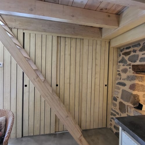 Intérieur rustique du gîte Le Four avec lambris bois, murs en pierre et escalier en bois