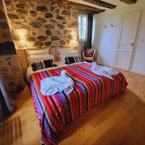 Deux lits jumeaux avec des couvertures rayées colorées dans une chambre en pierre du Mas De Rigoulac, Argences-en-Aubrac