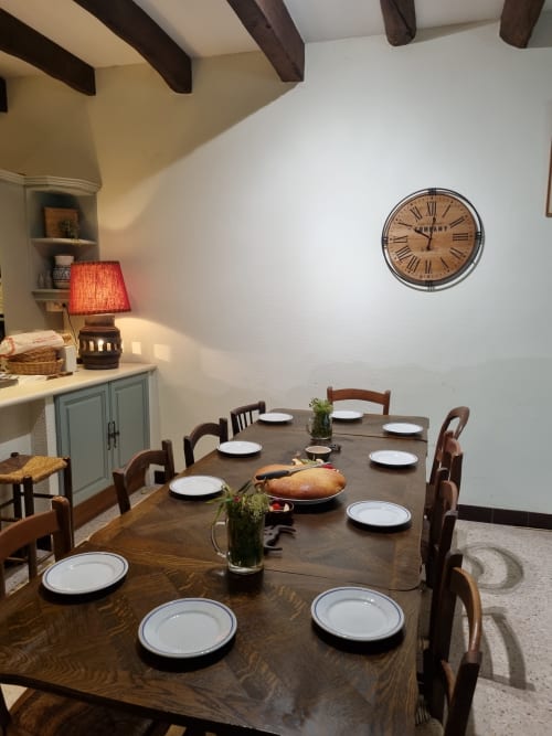 Elegant dining room at La Conciergerie De Franck villa in Boissieres with wooden table, period clock, and rustic beamed