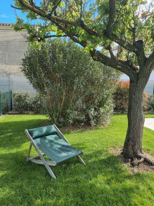 Teal lounger under mature tree in La Conciergerie De Franck's garden, Boissières villa with green lawn and olive shrub