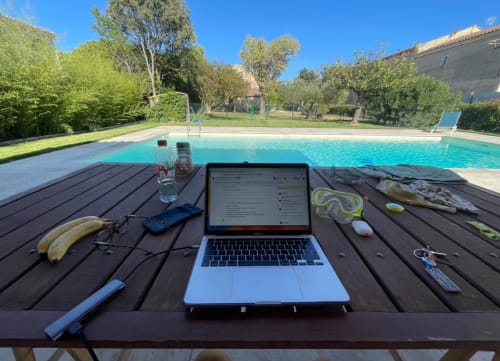 Laptop and pool accessories on wooden deck overlooking turquoise swimming pool at La Conciergerie De Franck villa in