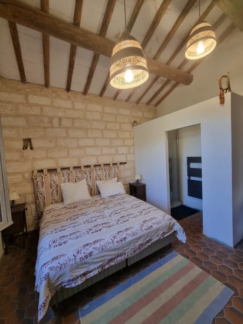 Rustic stone bedroom at La Conciergerie De Franck villa in Boissieres with exposed beams, woven pendant lights, and striped