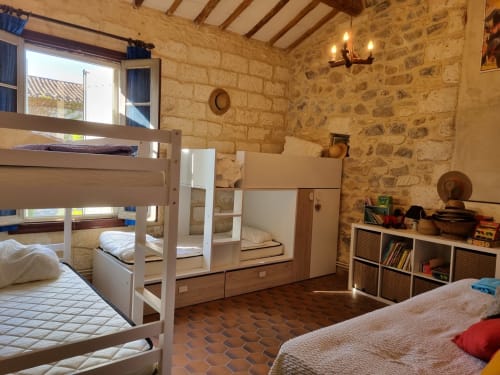 Rustic stone villa bedroom with bunk beds, terracotta tiles, and exposed beams in Boissieres
