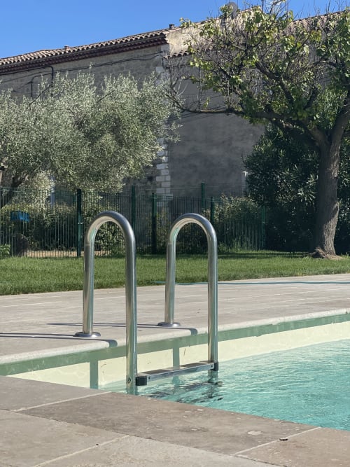 Piscine avec échelle métallique à la villa La Conciergerie De Franck à Boissieres, entourée de verdure luxuriante et de pierre